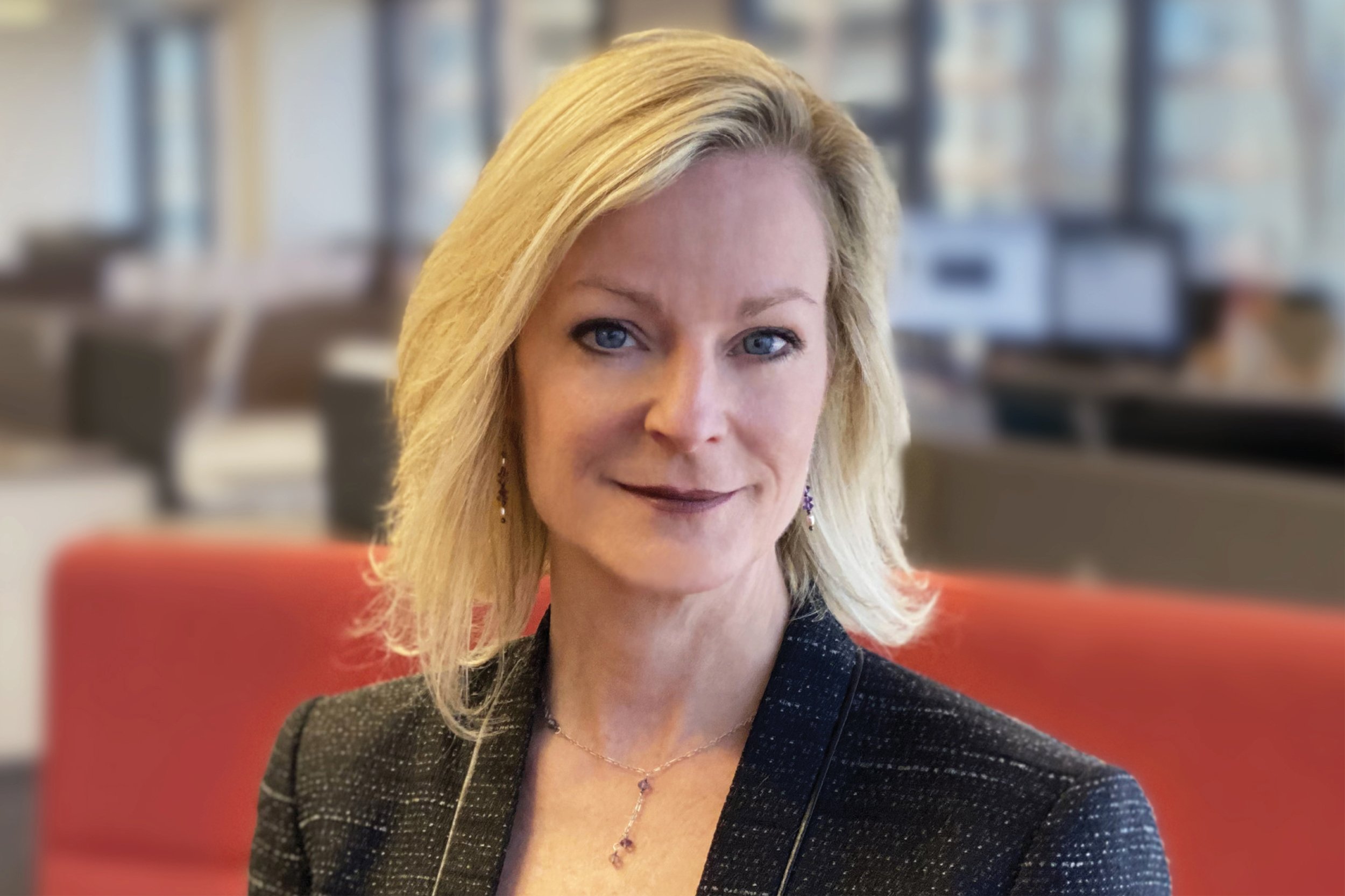 Portrait of Marsha Whitt, Vice President, wearing a black blazer and jewelry, sitting in a modern office with blurred background.