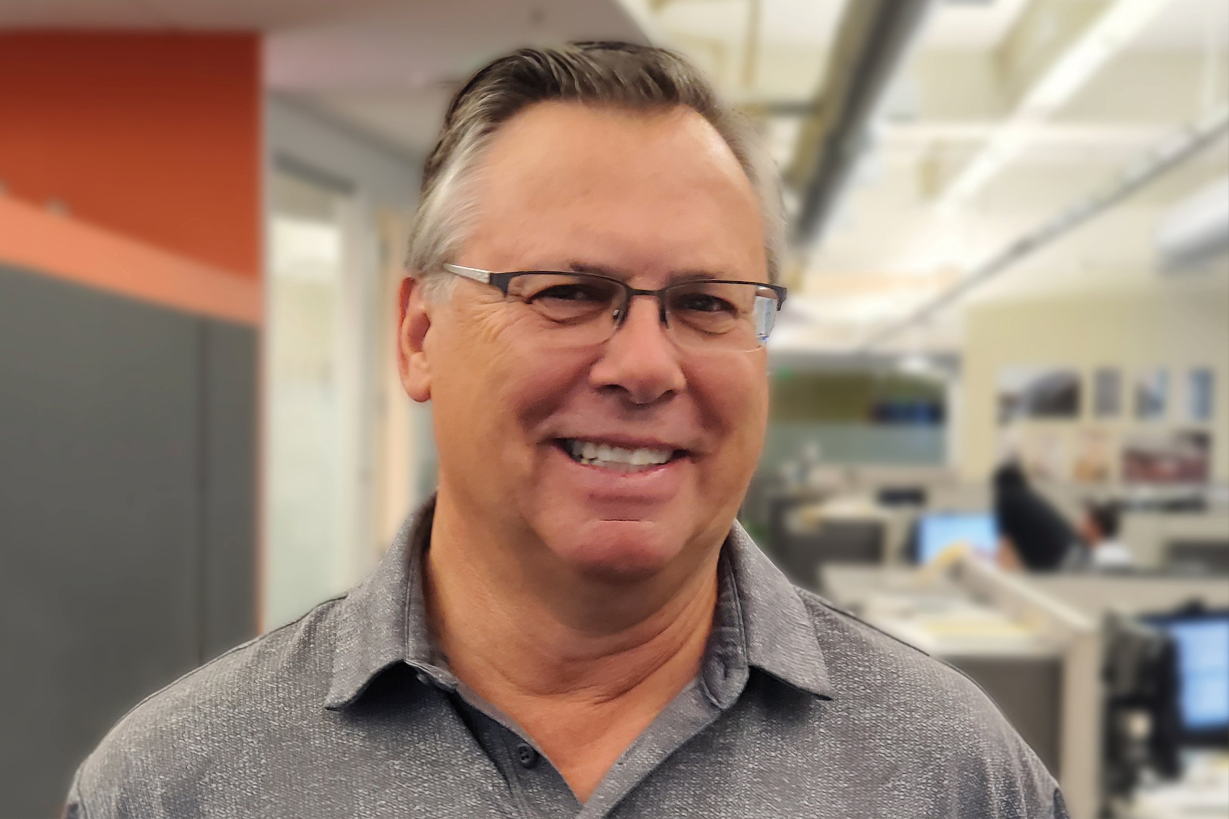 Smiling middle-aged man with glasses and gray hair in an office setting.